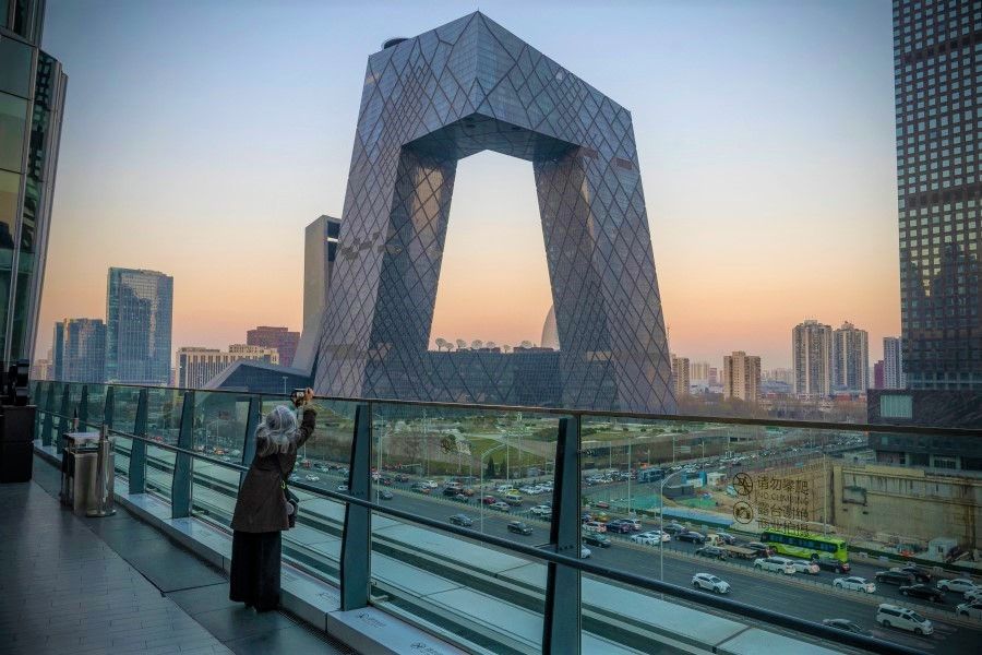 A woman takes a photograph of the China Central Television (CCTV) Tower in Beijing, China, on Monday, 13 Dec, 2021. Economists predict China will start adding fiscal stimulus in early 2022 after the country's top officials said their key goals for the coming year include counteracting growth pressures and stabilising the economy. (Andrea Verdelli/Bloomberg)