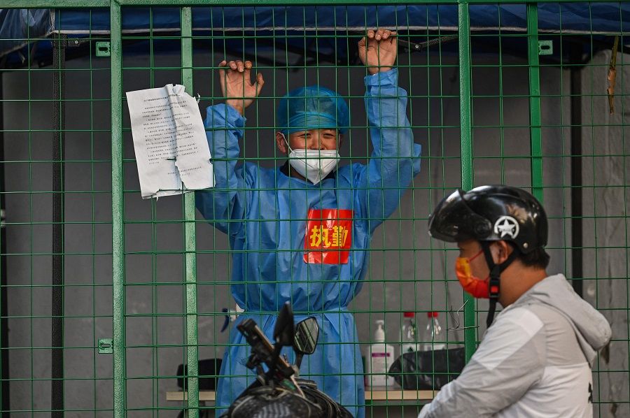 A worker wearing protective gear and standing behind a fence in a residential area under Covid-19 lockdown talks with a man on a scooter in the Xuhui district of Shanghai, China, on 16 June 2022. (Hector Retamal/AFP)
