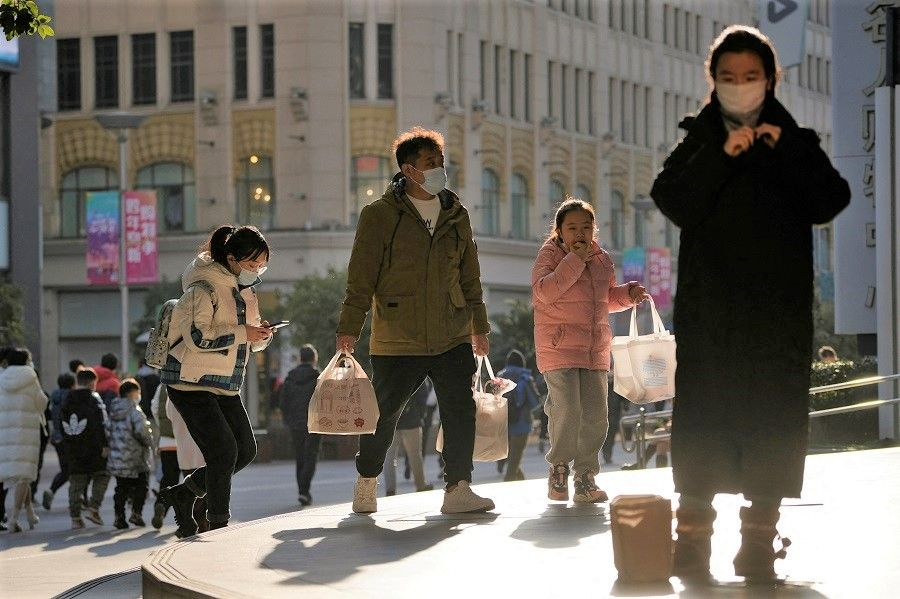 People wearing protective masks walk in a shopping district in Shanghai, China, 3 January 2023. (Aly Song/Reuters)
