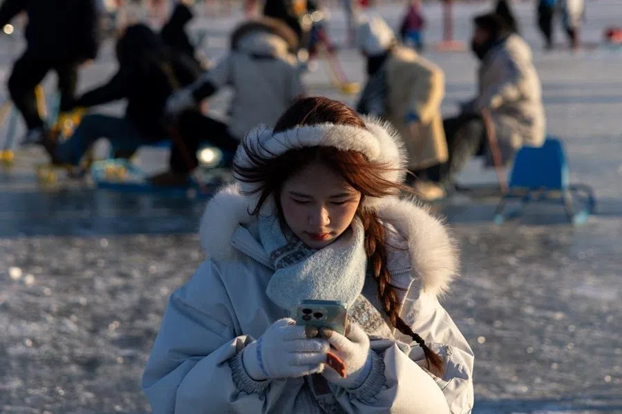 A young woman uses her smartphone at the frozen Kunming Lake ice rink at Summer Palace in Beijing, China, on 20 January 2026. (Maxim Shemetov/Reuters)