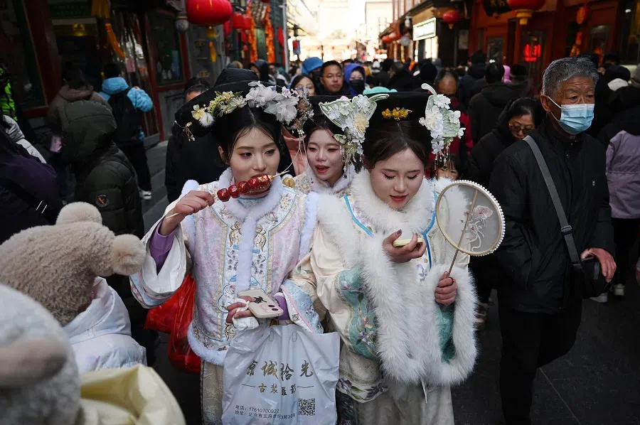 Three woman eat snack food as the walk through a popular shopping street wearing traditional clothing in Beijing, China, on 3 February 2025. (Greg Baker/AFP)