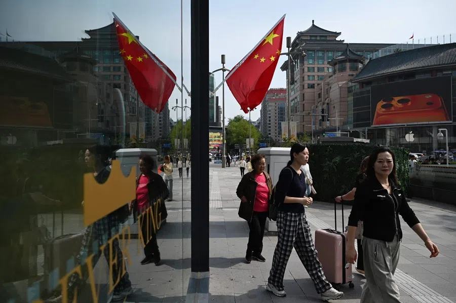 People walk outside a shopping mall during a week-long National Day holiday in Beijing on 7 October 2025. (Greg Baker/AFP)