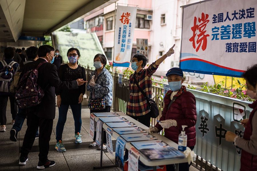 A man (left) speaks to a lady looking after a stall with a banner that reads "Support the NPC's Decision on Improving Elections" in Hong Kong on 11 March 2021, after China's parliament voted overwhelmingly for changes to Hong Kong's electoral system. (Anthony Wallace/AFP)