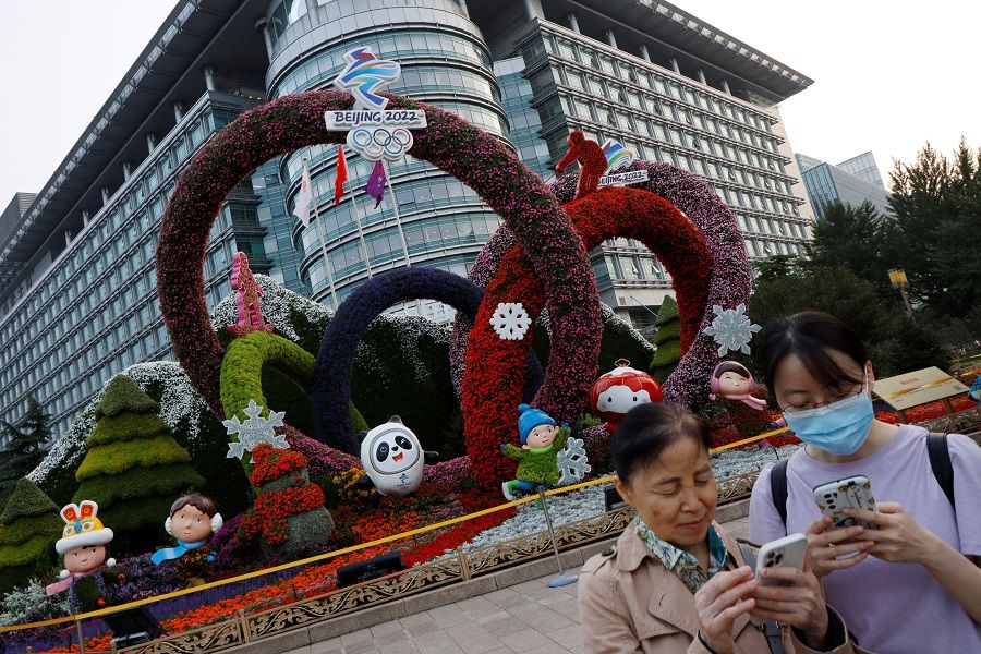 People check their phones near a Beijing 2022 Winter Olympics-themed floral installation set up ahead of the Chinese National Day, in Beijing, China, 30 September 2021. (Florence Lo/Reuters)
