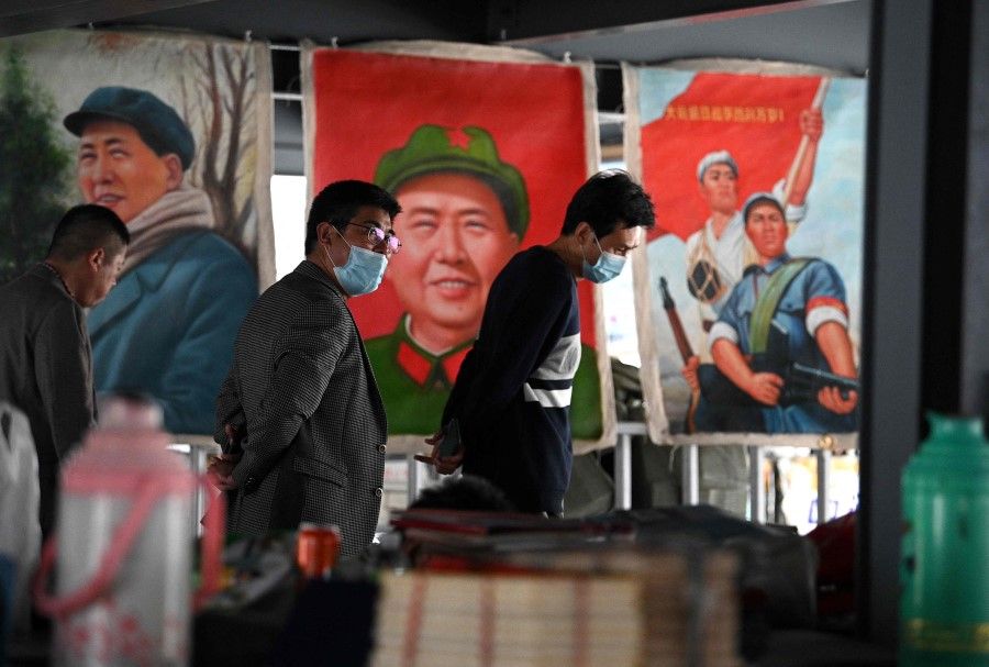 People walk past posters of the late Chinese Communist leader Mao Zedong at a stall in the Panjiayuan antique market in Beijing, China on 25 April 2021. (Noel Celis/AFP)