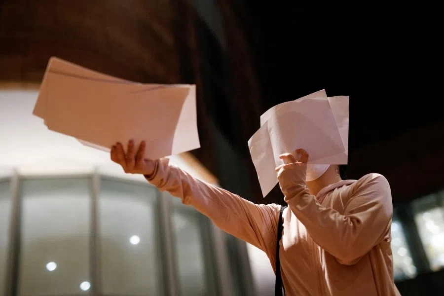 A woman hands out sheet of paper in protest over Covid-19 restrictions in mainland China, during a commemoration of the victims of a fire in Urumqi, at the University of Hong Kong (HKU), in Hong Kong, China, 29 November 2022. (Tyrone Siu/Reuters)