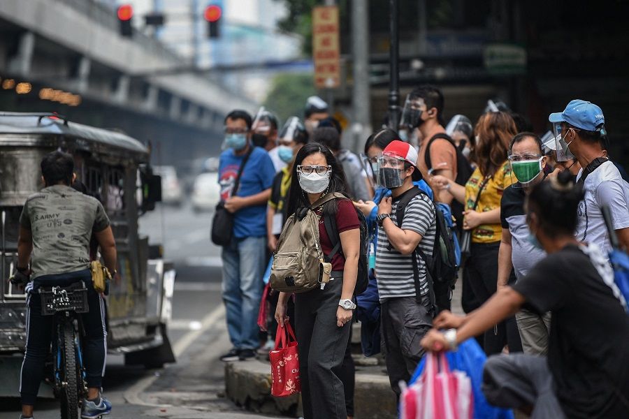 People wearing face masks and shields to protect themselves against the Covid-19 coronavirus wait for their transport on a street in Manila, the Philippines, on 7 September 2021. (Ted Aljibe/AFP)
