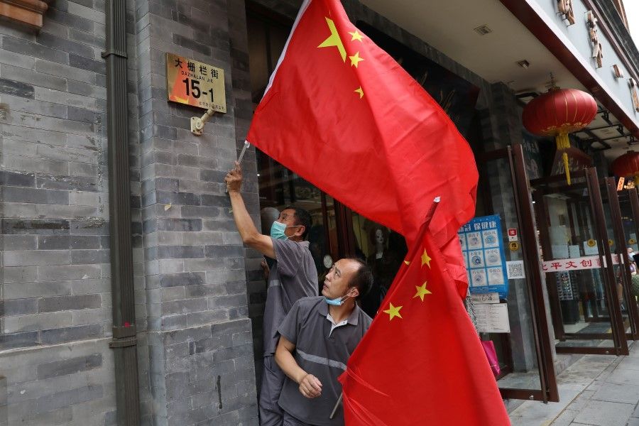 Workers set Chinese national flags on a shopping street ,ahead of a rehearsal for the celebrations to mark the 100th founding anniversary of the Communist Party of China, in Beijing, China, 26 June 2021. (Tingshu Wang/Reuters)