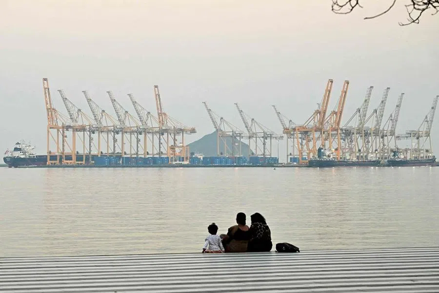 A family sits against the backdrop of a dockyard off coast city of Fujairah, in the Strait of Hormuz in the northern Emirate on 25 February 2026. (Giuseppe Cacace/AFP)