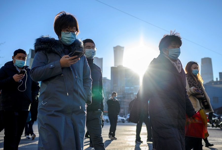 People wearing face masks walk along a street during a rush hour in Bejing on 16 December 2020. (Noel Celis/AFP)