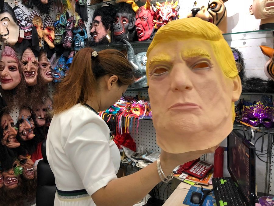 A vendor holding up a Donald Trump latex mask that she sells.
