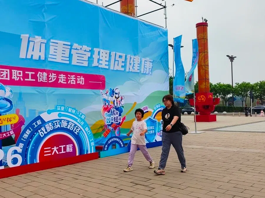 People walk past promotional material on a weight management activity at a park in Beijing.