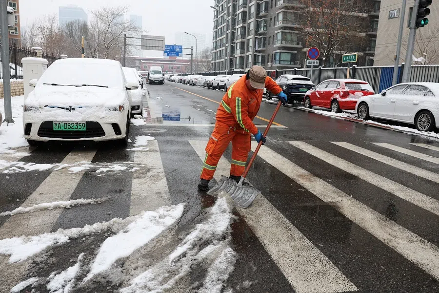 A cleaning worker shovels snow on a street in Beijing, China, on 13 December 2023. (Tingshu Wang/Reuters)