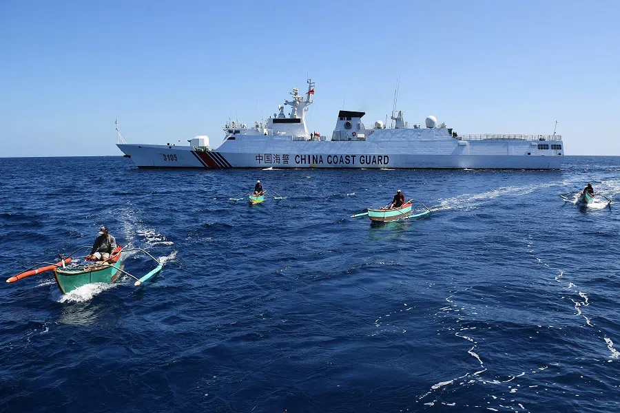 This photo taken on 15 February 2024 shows Filipino fishermen aboard their wooden boats sailing past a Chinese coast guard ship near the China-controlled Scarborough Shoal, in disputed waters of the South China Sea.