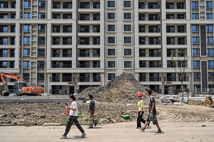 This picture taken on 2 June 2023 shows workers walking past apartment buildings under construction in a compound in Ningbo, Zhejiang province, China. (Hector Retamal/AFP)