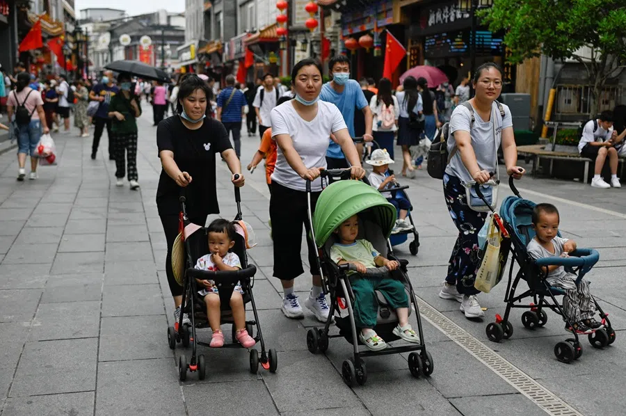 People push baby strollers along a business street in Beijing on 13 July 2021. (Wang Zhao/AFP)