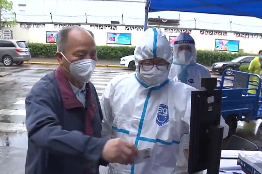 A screen grab of a video showing a health worker helping an elderly man scan his identification card. (Weibo)