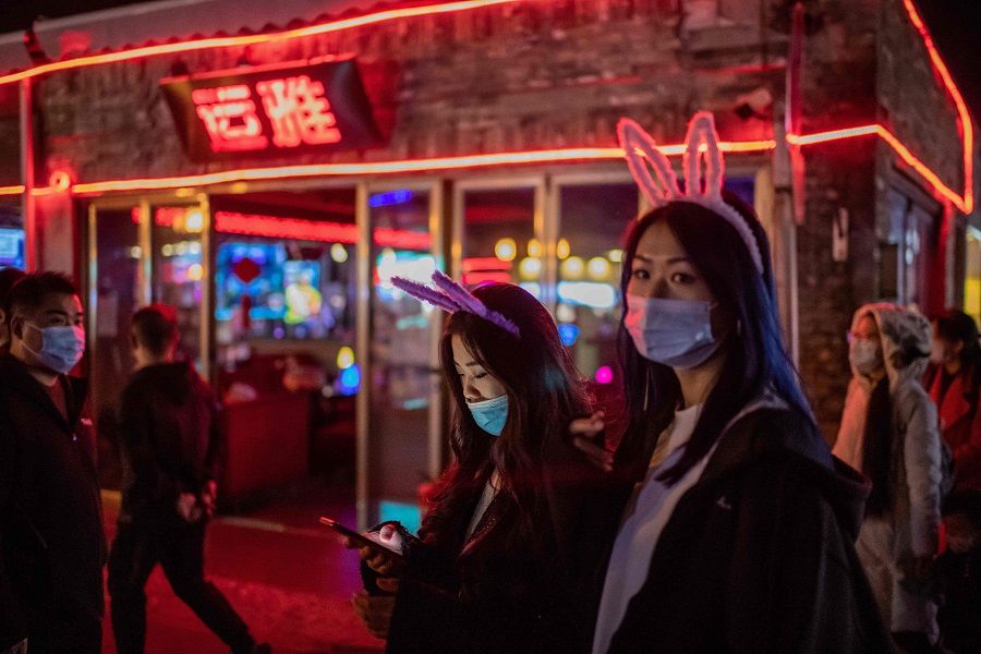 A young woman (centre) browses her smartphone while walking with a friend along a street in Beijing on 28 October 2020. (Nicolas Asfouri/AFP)