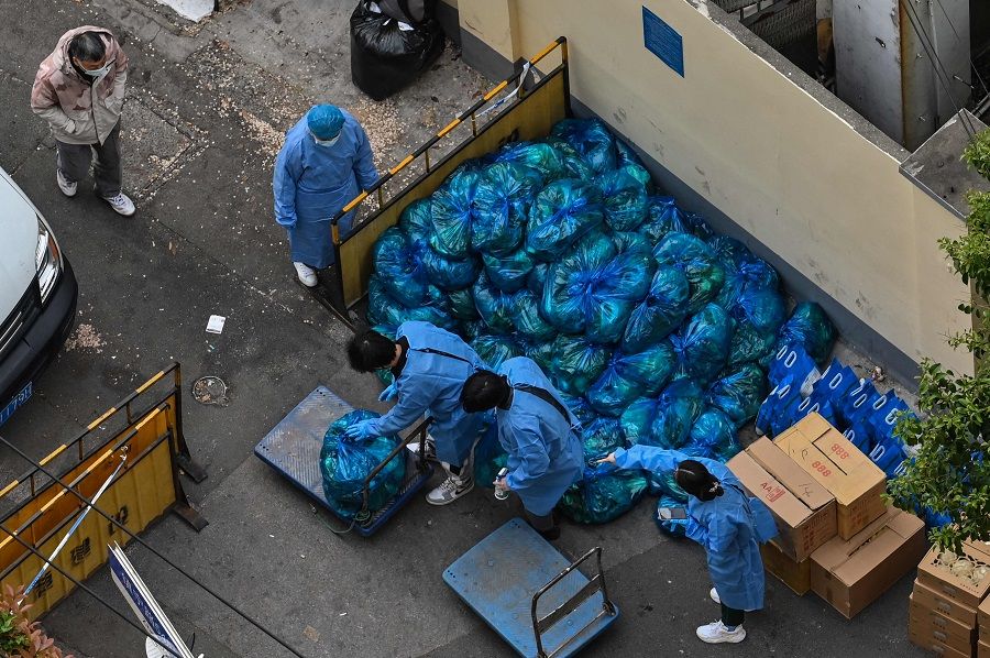This photo taken on 16 April 2022 shows workers in protective gear sorting bags of vegetables to be delivered to residents of a neighbourhood during a Covid-19 coronavirus lockdown in the Jing'an district of Shanghai on 16 April 2022. (Hector Retamal/AFP)