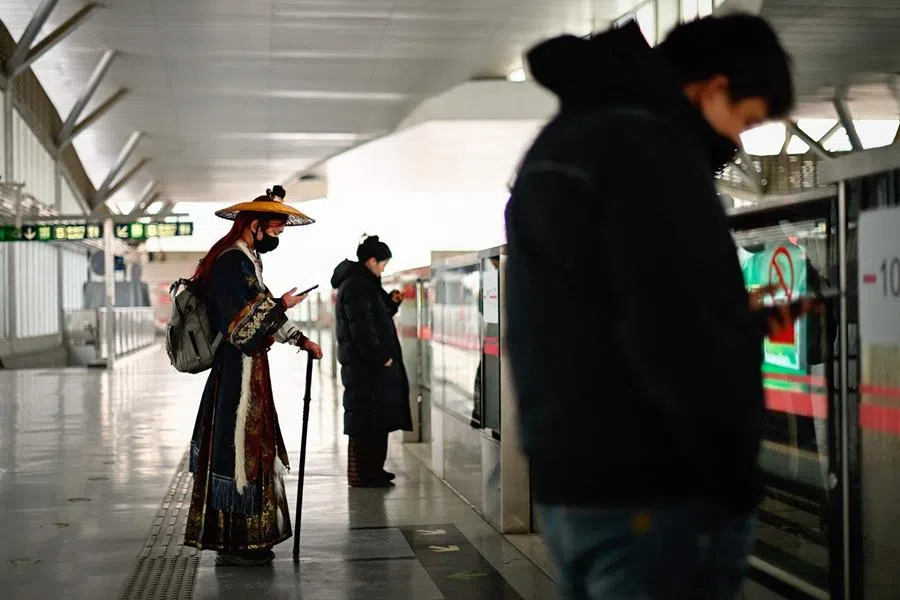 People use their mobile phones as they wait for a train at a subway station in Beijing on 18 January 2026. (Wang Zhao/AFP)