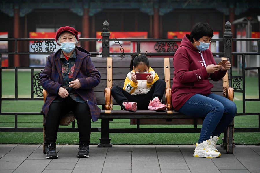 A girl uses a mobile phone as she rests on a bench in Beijing, China, on 4 March 2021. (Wang Zhao/AFP)