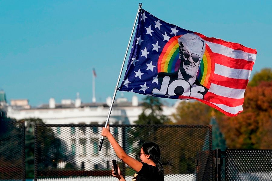 In this file photo taken on 7 November 2020, a woman waves a Joe Biden flag as people celebrate on Black Lives Matter Plaza across from the White House in Washington, DC, after Biden was declared the winner of the 2020 presidential election. (Alex Edelman/AFP)