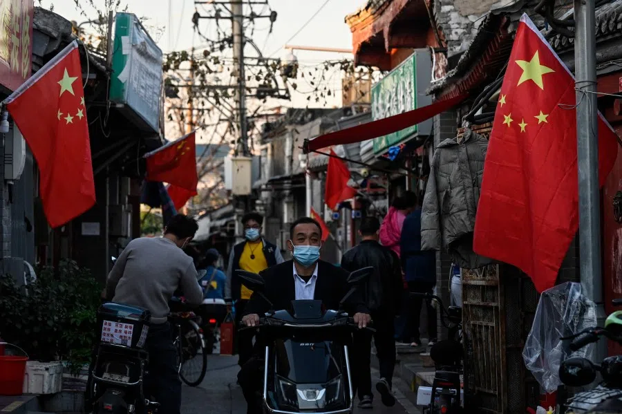 People ride past China national flags along an alley ahead of the 20th Communist Party Congress, in Beijing on 11 October 2022. (ade Gao/AFP)
