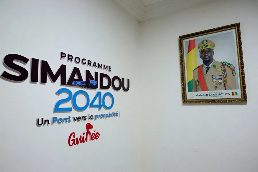 A portrait of Guinean leader Mamadi Doumbouya hangs on a wall next to a writing that reads "Simandou 2040 programme, a bridge to prosperity!" in Conakry, Guinea, on 6 November 2025. (Luc Gnago/Reuters)