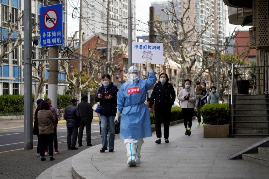 A worker in a protective suit shows a QR code to residents lining up for nucleic acid testing, as the second stage of a two-stage lockdown to curb the spread of the coronavirus disease (COVID-19) begins in Shanghai, China, 1 April 2022. (Aly Song/Reuters)