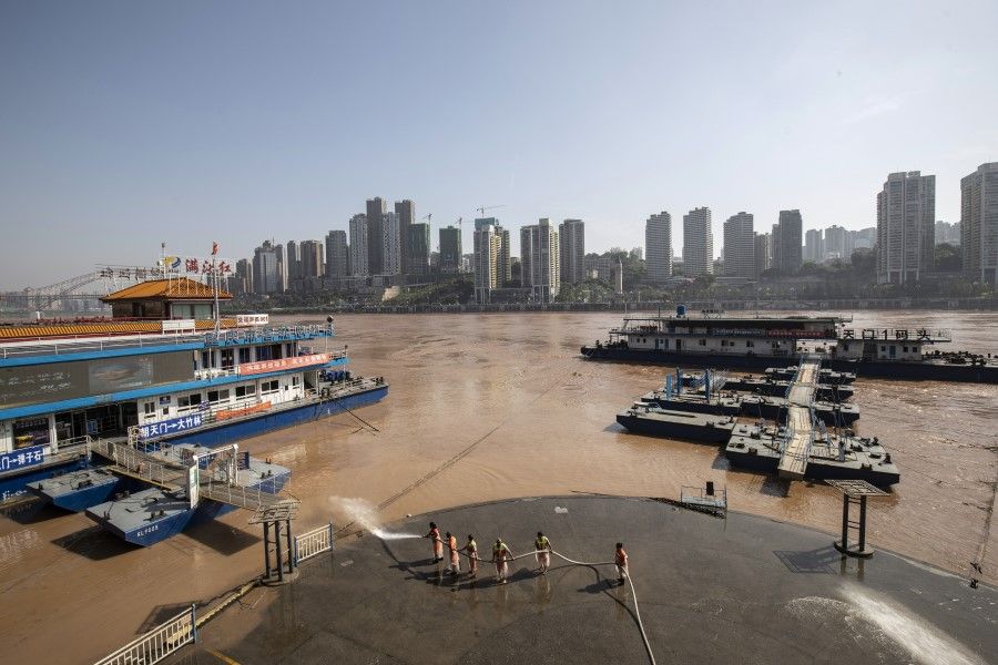 Workers use a fire hose to wash away mud left by receded floodwaters off the Chaotianmen docks in Chongqing, 28 July 2020. (Qilai Shen/Bloomberg)