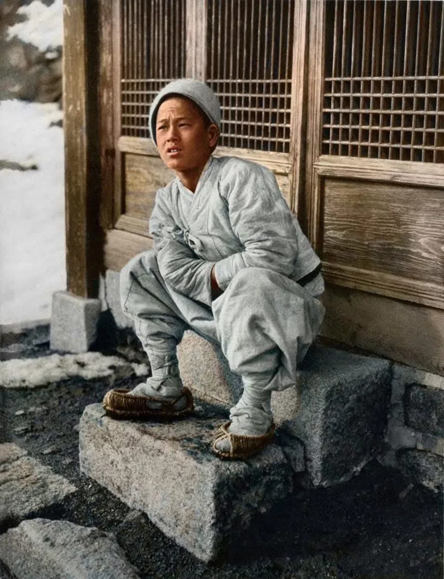 A young boy sitting in a doorway, circa 1900.