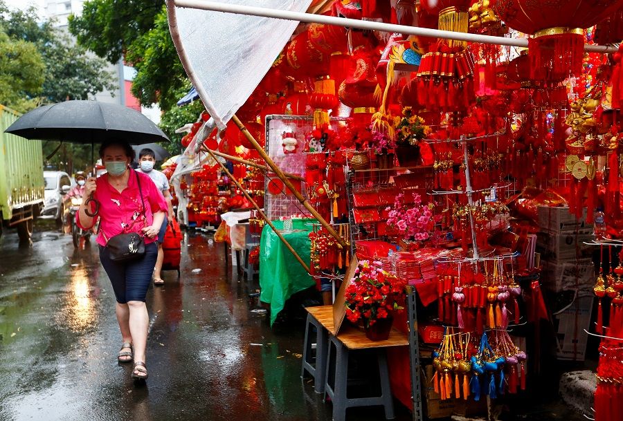 A woman wearing a protective mask carries an umbrella as she walks past a stall selling decorations at a street market ahead of the Lunar New Year, in Jakarta, Indonesia, 4 February 2021. (Ajeng Dinar Ulfiana/Reuters)