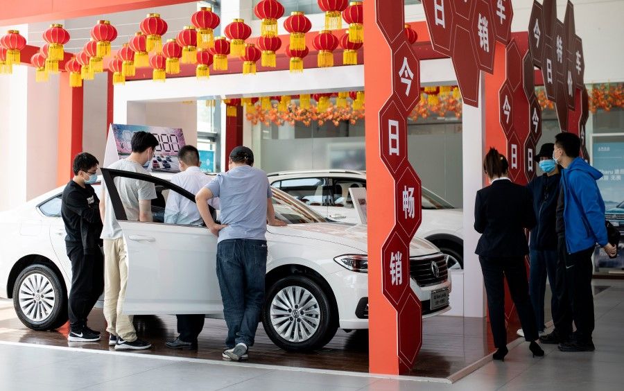 This photo taken on 10 May 2020 shows people looking at Volkswagen cars on display at a showroom in Beijing. (Noel Celis/AFP)