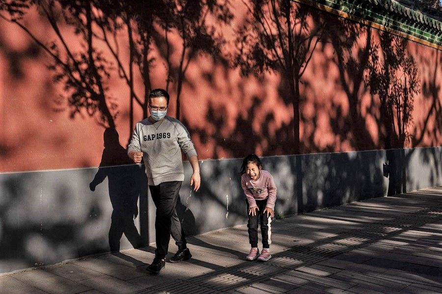 A girl reacts and laughs as she loses a game of rock-paper-scissors with her father (left) on a street outside the Forbidden City in Beijing, China on 1 May 2021. (Nicolas Asfouri/AFP)