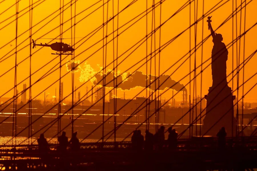 The sun sets behind the Statue of Liberty as people walk on the Brooklyn Bridge in New York on 6 February 2024. (Charly Triballeau/AFP)