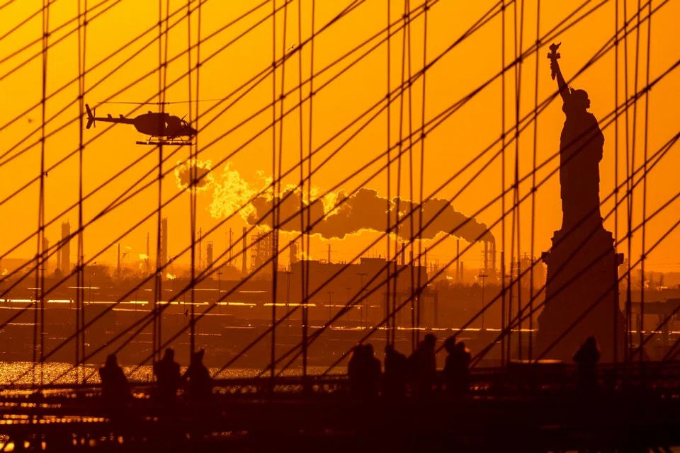 The sun sets behind the Statue of Liberty as people walk on the Brooklyn Bridge in New York on 6 February 2024. (Charly Triballeau/AFP) (AFP)