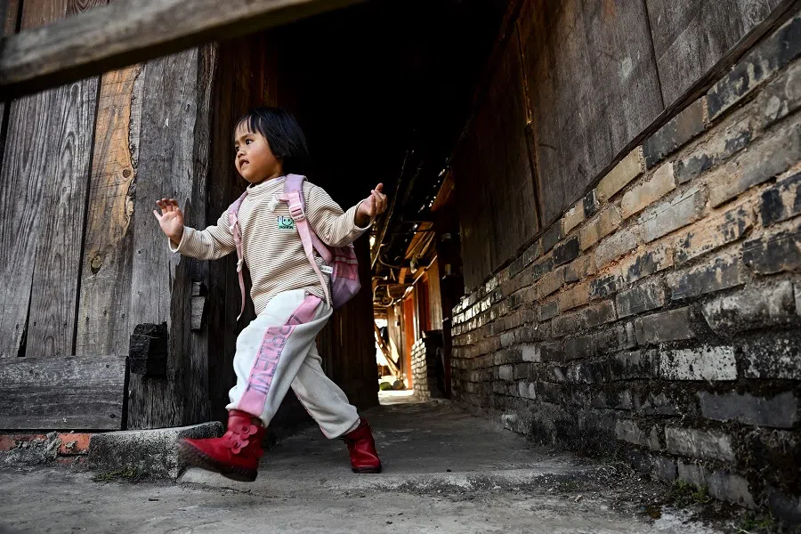 This photo taken on 10 January 2023 shows an ethnic Blang girl running along an alley in Wengji village on Jingmai mountain in Pu'er City in Yunnan province, China. (Noel Celis/AFP)