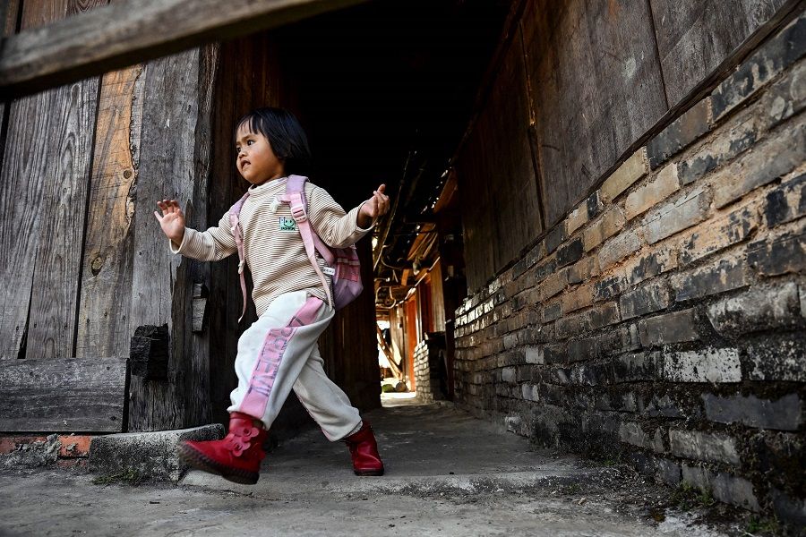 This photo taken on 10 January 2023 shows an ethnic Blang girl running along an alley in Wengji village on Jingmai mountain in Pu'er City in Yunnan province, China. (Noel Celis/AFP)