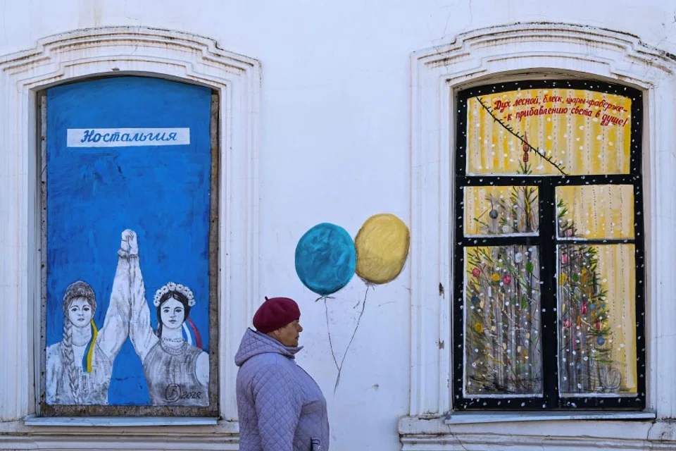 A woman walks past graffiti in Borovsk, some 100 km south-west of Moscow, 14 April 2022. (AFP)