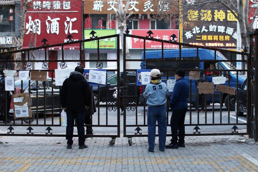 This photo taken on 5 April 2022 shows residents reading boards with phone numbers of stores that can deliver food at the entrance of a residential area, which is restricted due to the spread of Covid-19 in Shenyang in China's northeastern Liaoning province. (AFP)