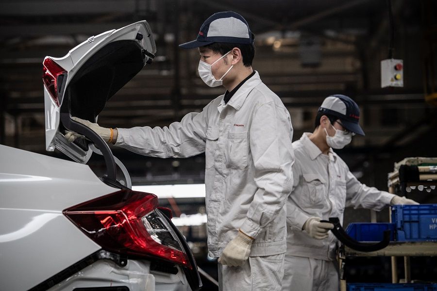This photo taken on 23 March 2020 shows employees wearing face masks working on an assembly line at an auto plant of Dongfeng Honda in Wuhan, Hubei, China. (STR/AFP)