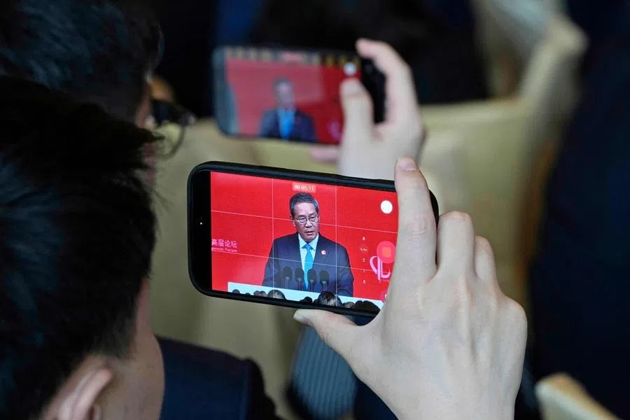 Chinese Premier Li Qiang is seen on phone screen as attendees record from a big screen live broadcasting his speech at the opening of the China Development Forum 2026 held at the Diaoyutai State Guesthouse in Beijing on 22 March 2026. (Ng Han Guan/AFP)