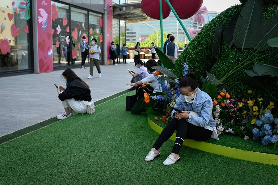 People use their mobile phones outside a mall at a business district in Beijing, China, on 16 May 2022. (Wang Zhao/AFP)