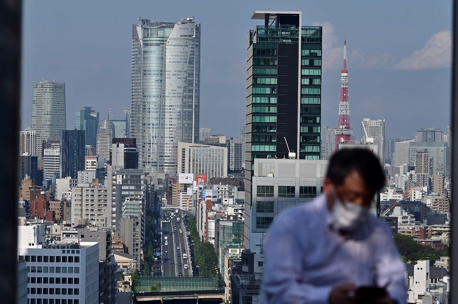 A man sitting on a rooftop looks at his phone before the city skyline in Tokyo on 8 June 2020. (Charly Triballeau/AFP)