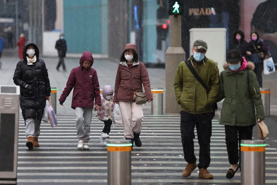 People wearing face masks walk past a street amid snowfall at a shopping area in Beijing, China, 17 March 2022. (Tingshu Wang/Reuters)