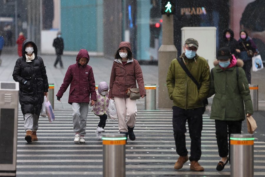 People wearing face masks walk past a street amid snowfall at a shopping area in Beijing, China, 17 March 2022. (Tingshu Wang/Reuters)