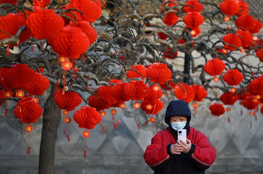 A woman takes a picture next a tree decorated with paper lanterns at the entrance of a park in Beijing, China, on 26 January 2023. (Wang Zhao/AFP)