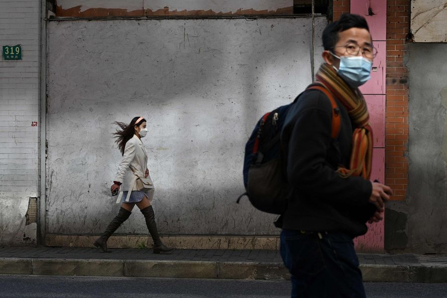 People wearing protective face masks walk along a street in Shanghai on 17 February 2020. (Noel Celis/AFP)
