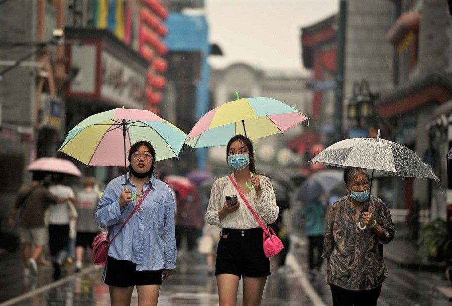 People use umbrellas as they walk along Qianmen street in Beijing, China, on 18 August 2022. (Noel Celis/AFP)