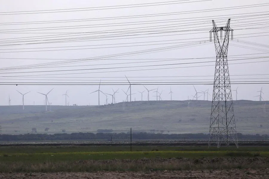 An electricity pylon and powers lines are seen against a backdrop of wind turbines in Zhangjiakou, Hebei province, China, 15 July 2021.
